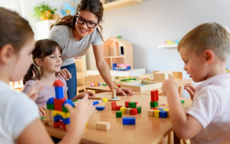 Preschool teacher with children playing with colorful wooden didactic toys at kindergarten